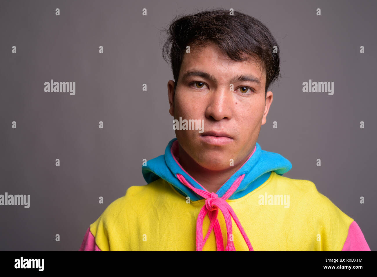 Young Asian man wearing colorful hoodie contre l'arrière-plan gris Banque D'Images