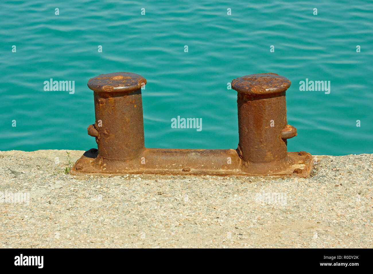 Rusty acier amarrage double bitt sur un fragment d'ancienne jetée en béton sur le fond de la mer turquoise de l'eau dans le calme Banque D'Images