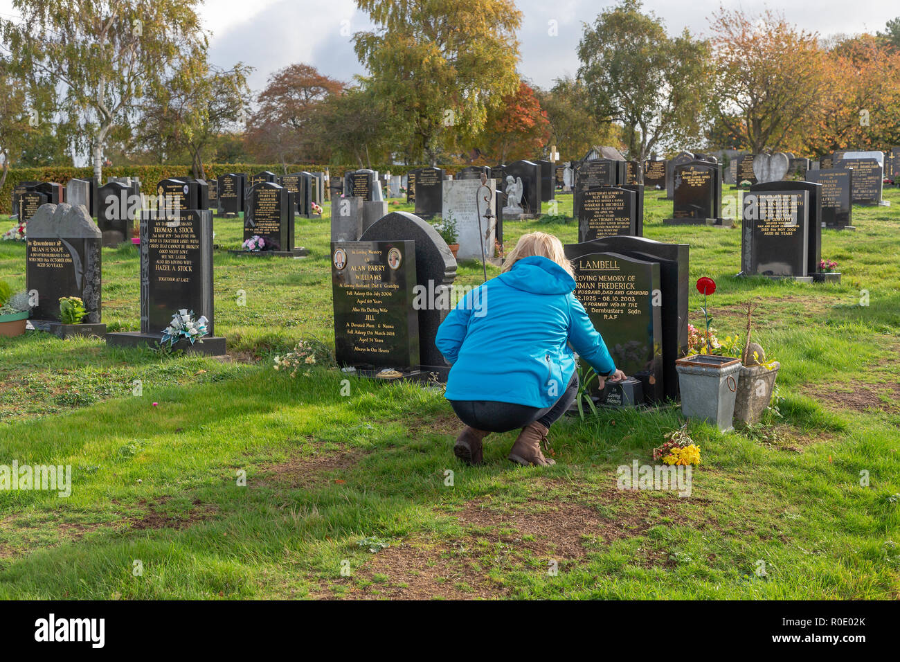 Blonde mature dame supprime les fleurs mortes provenant d'une tombe et dit une prière pour son père Banque D'Images