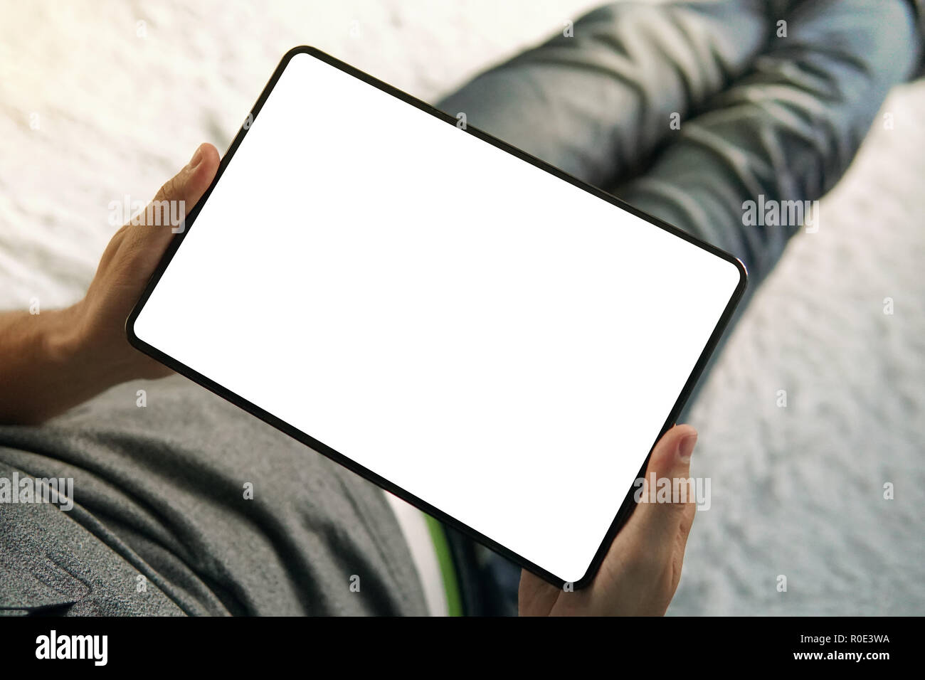 Une moitié inférieure d'un homme assis sur le lit à la recherche jusqu'à l'écran vide de un comprimé. Un jeune homme est assis à la maison et regarde la tablette sc Banque D'Images