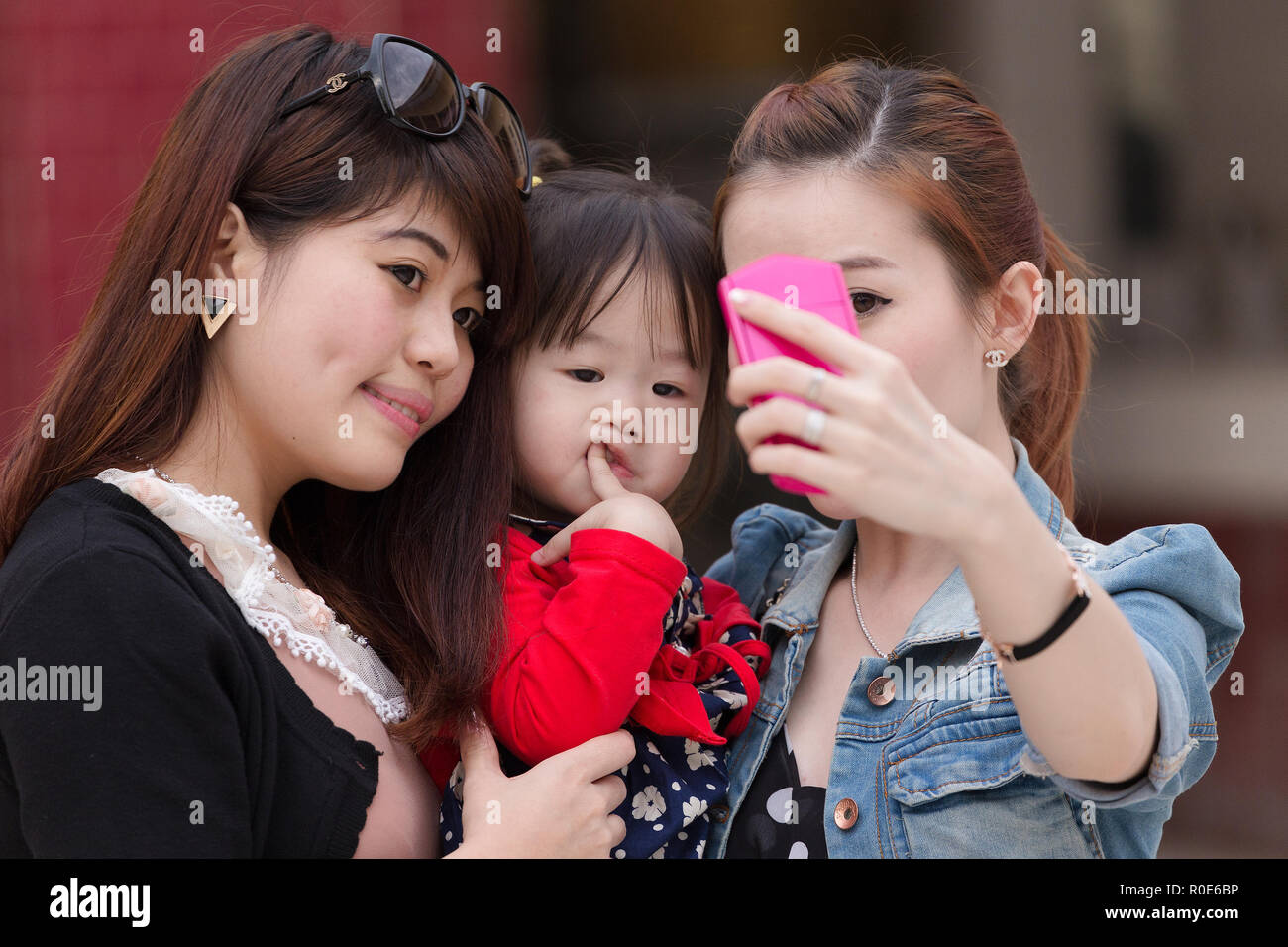 MANDALAY, Myanmar, le 16 janvier 2015 : les femmes coréennes sont le tournage d'un autoportrait (selfies) avec une drôle de petite fille s'ennuie dans une rue de Mandalay, Myanmar Banque D'Images