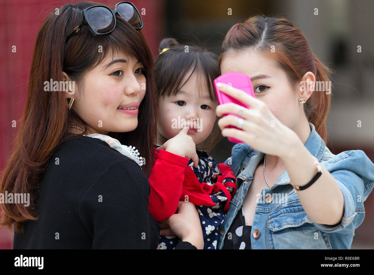 MANDALAY, Myanmar, le 16 janvier 2015 : les femmes coréennes sont le tournage d'un autoportrait (selfies) avec une drôle de petite fille s'ennuie dans une rue de Mandalay, Myanmar Banque D'Images