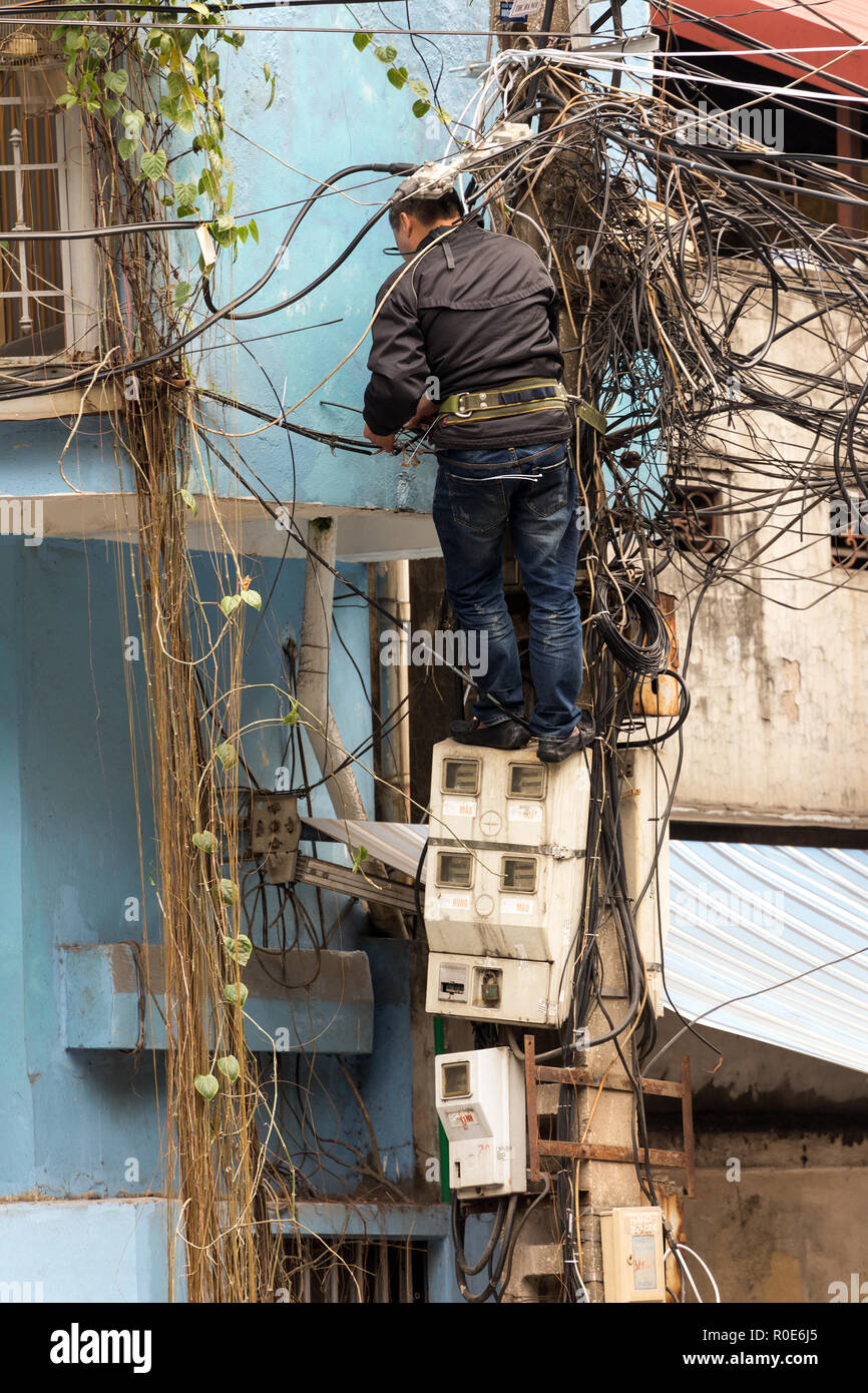 HANOI, Vietnam, 16 décembre 2014 : Un technicien debout sur les compteurs d'électricité est la réparation ou vérification de l'installation électrique en désordre dans la ville réseau Banque D'Images