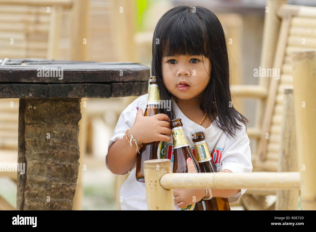 KO Phangan, Thaïlande, le 21 février 2011 : Une petite fille est la tenue de trois bouteilles de bières pour débarrasser la table du restaurant de son parent dans l'Ko Pha Banque D'Images