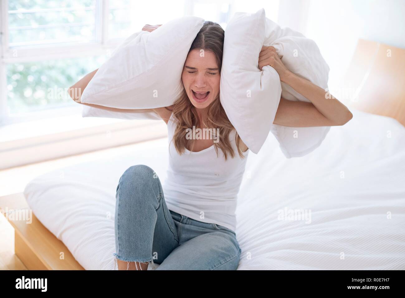 Jeune femme tenant un oreiller sur ses oreilles et crier. Banque D'Images
