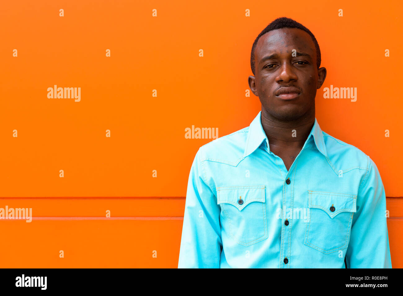 Les jeunes d'Afrique noire man leaning against orange mur peint Banque D'Images