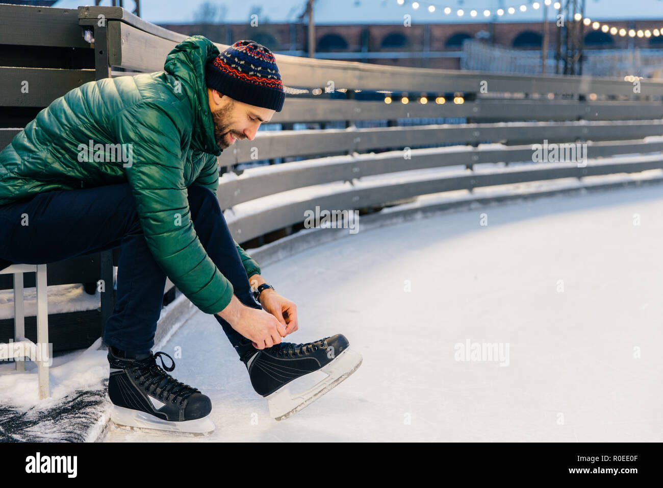 Les gens, sport d'hiver, loisirs concept. Ravissant sourire homme chausse ses patins, aller à l'anneau de glace sur la pratique, être en bonne humeur, aime l'hiver et g Banque D'Images