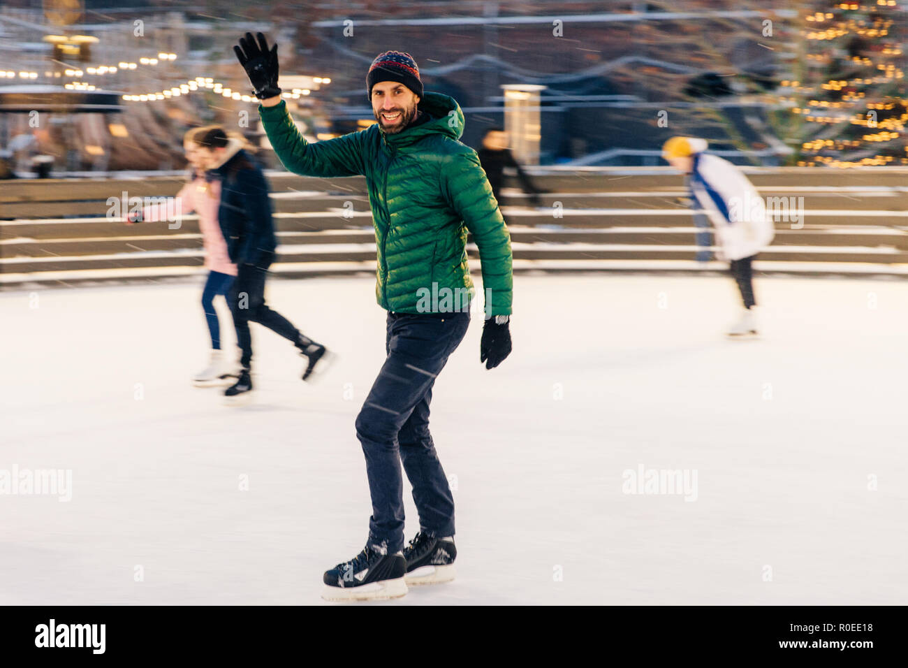 Heureux homme vagues avec la main, comme son ami avis sur patinoire, ont le désir de patiner ensemble, se réjouit réunion, a bon temps et l'humeur, divertit Banque D'Images