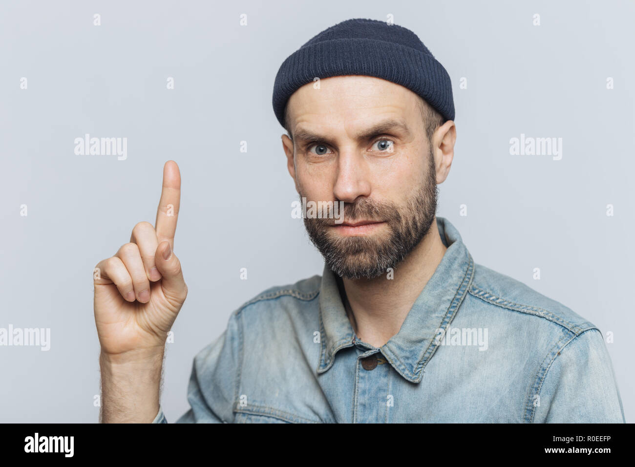 Tourné à l'intérieur de handsome man with regard sérieux, a belle apparence, épaisse barbe avec moustache, porte des vêtements à la mode, soulève que ge figer avant Banque D'Images