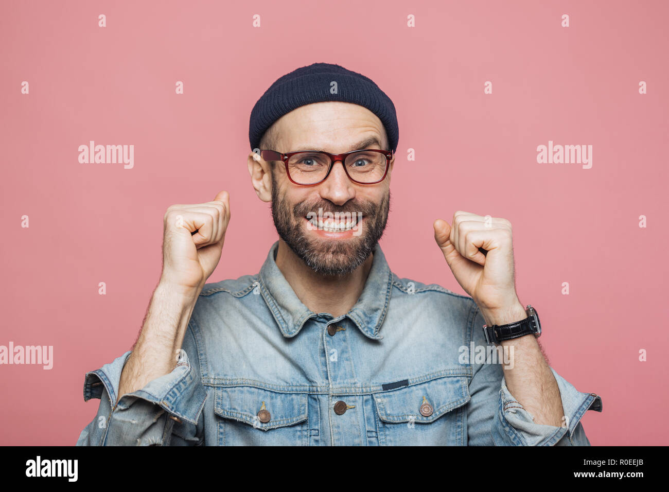 Heureux homme barbu avec des yeux bleus et l'expression joyeuse serre les poings, se sent pour être gagnant, témoigne de positivité, isolé sur fond rose Banque D'Images