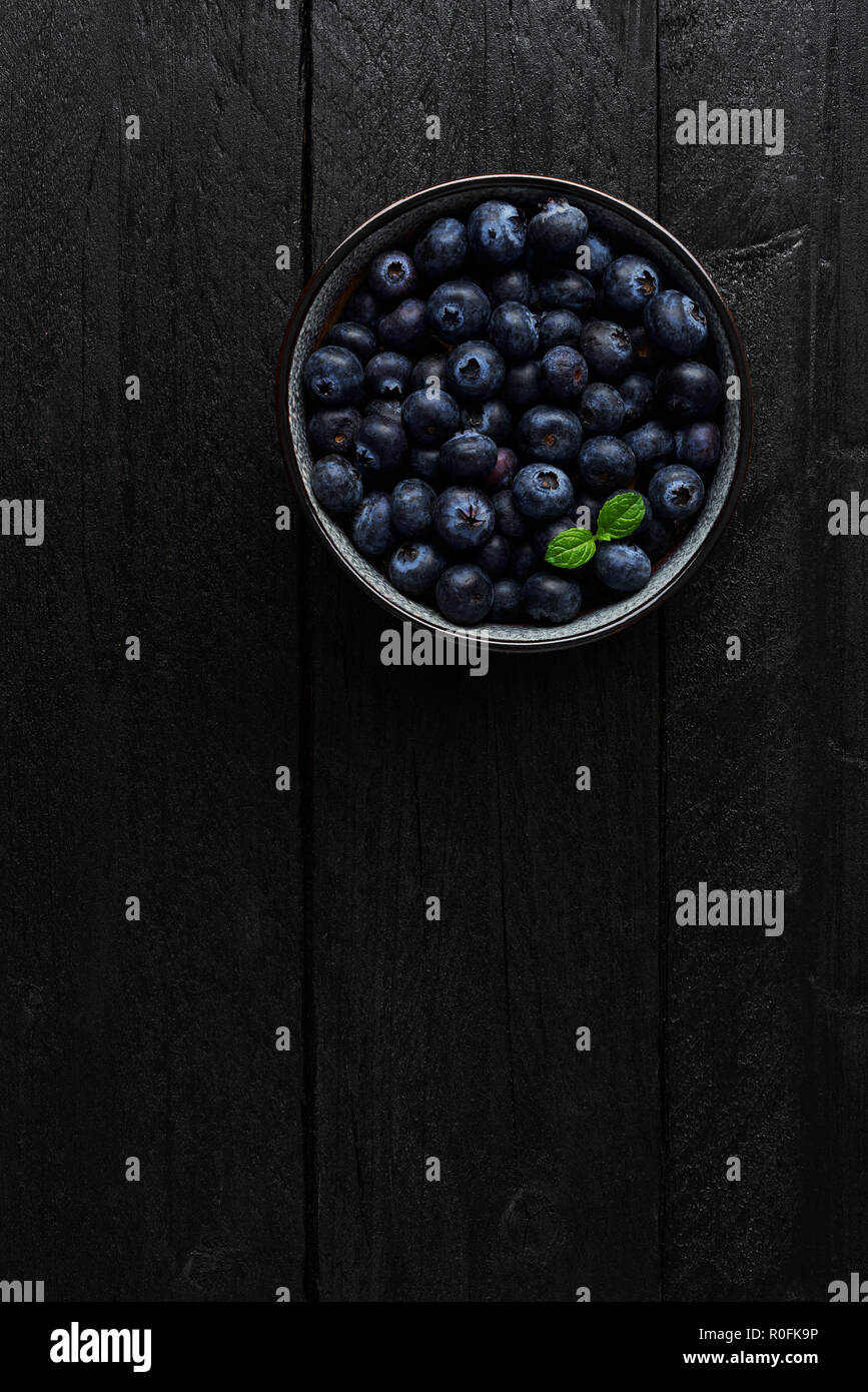 Vue de dessus de bleuets dans un bol avec feuille de menthe fraîche sur fond de bois noir avec copie espace. Banque D'Images