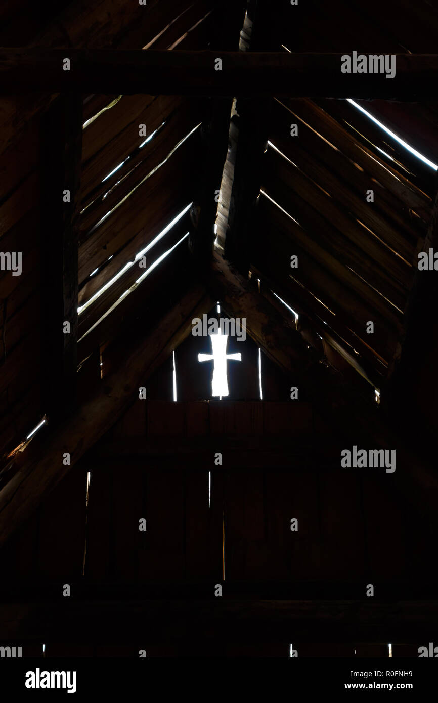 Trou en forme de croix de lumière dans une pièce sombre sur le vieux bois mur près de toit. Banque D'Images