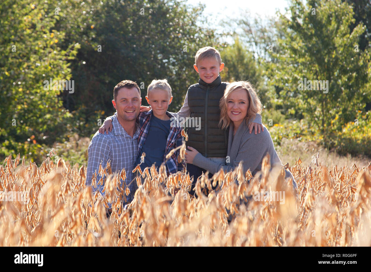 Belle blonde, famille avec une mère et un père et deux garçons, s'accroupit dans un champ pour une photo de famille Banque D'Images