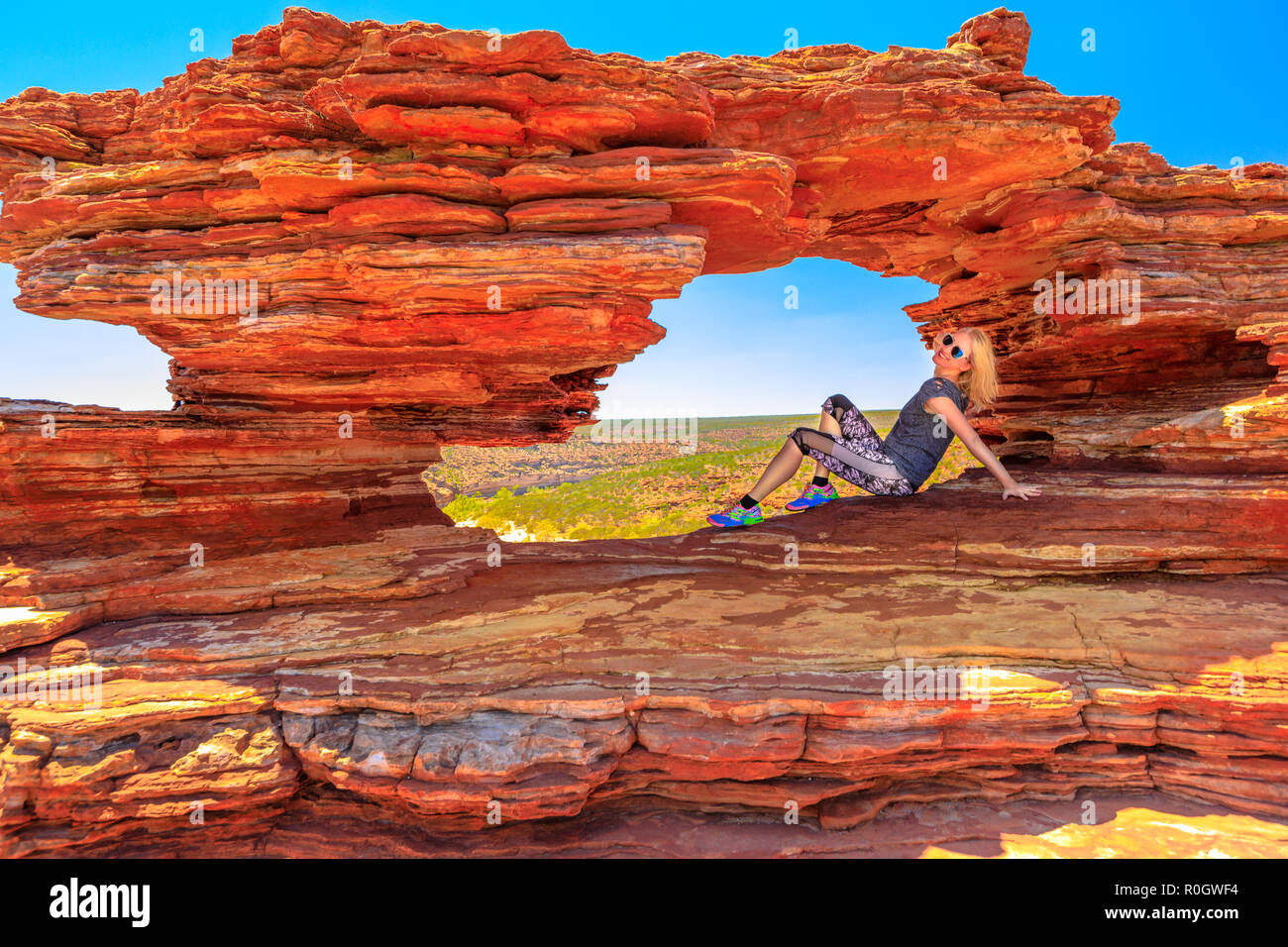 Femme blonde heureux assis à l'intérieur de l'icône rock arch en grès rouge de la fenêtre de la nature, le Parc National de Kalbarri. Jeune fille de race blanche dans l'ouest de l'Australie. Australia Travel concept liberté Banque D'Images