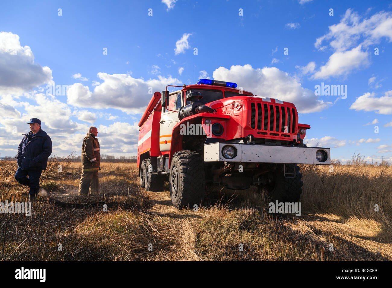 Camion rouge Ural et les pompiers sont sur le terrain avec l'herbe décolorée sur fond de ciel bleu et nuages. Concept de la masculinité, les conditions de travail con Banque D'Images