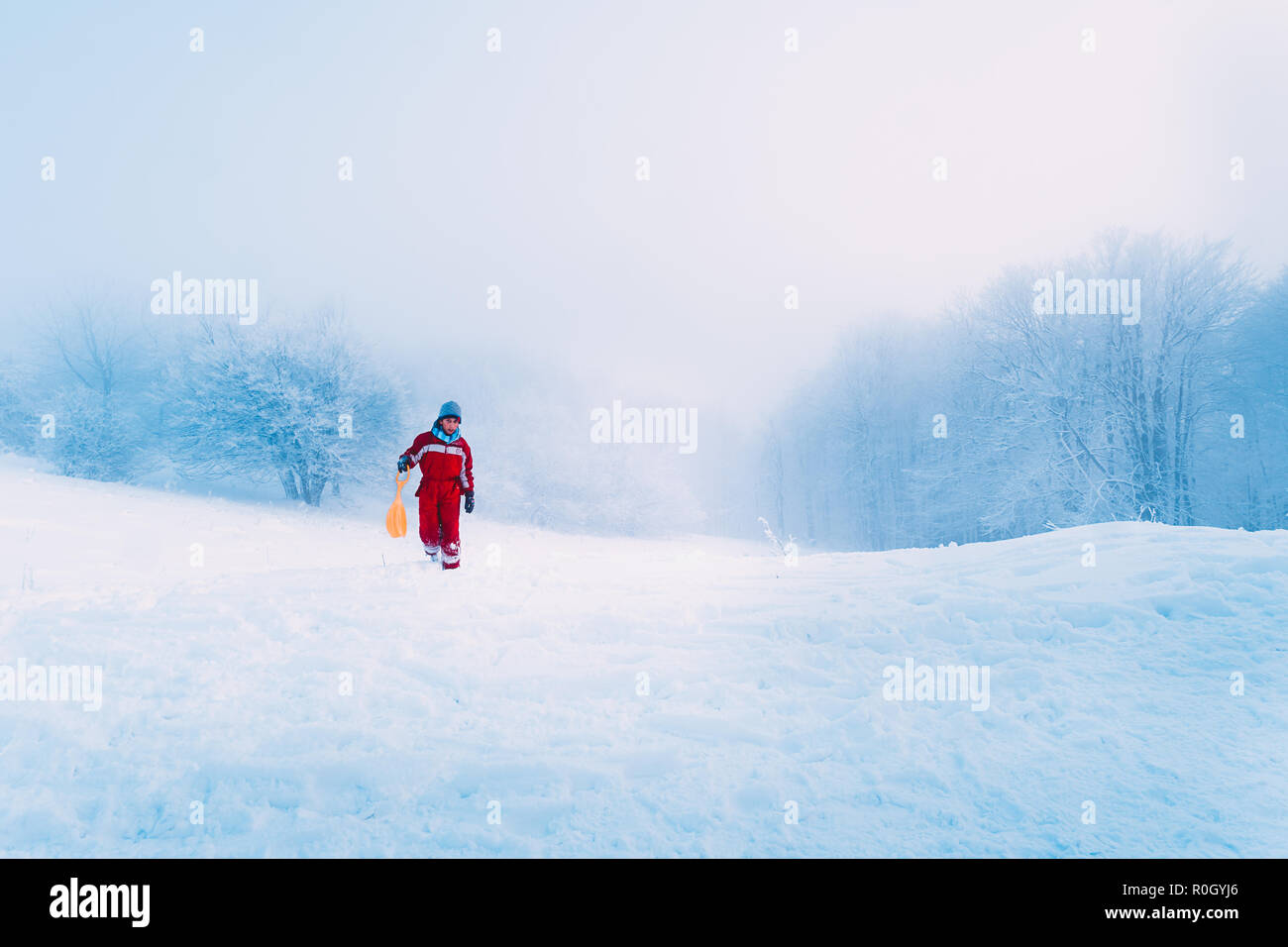 Un petit garçon avec son traîneau dans les montagnes enneigées. Banque D'Images