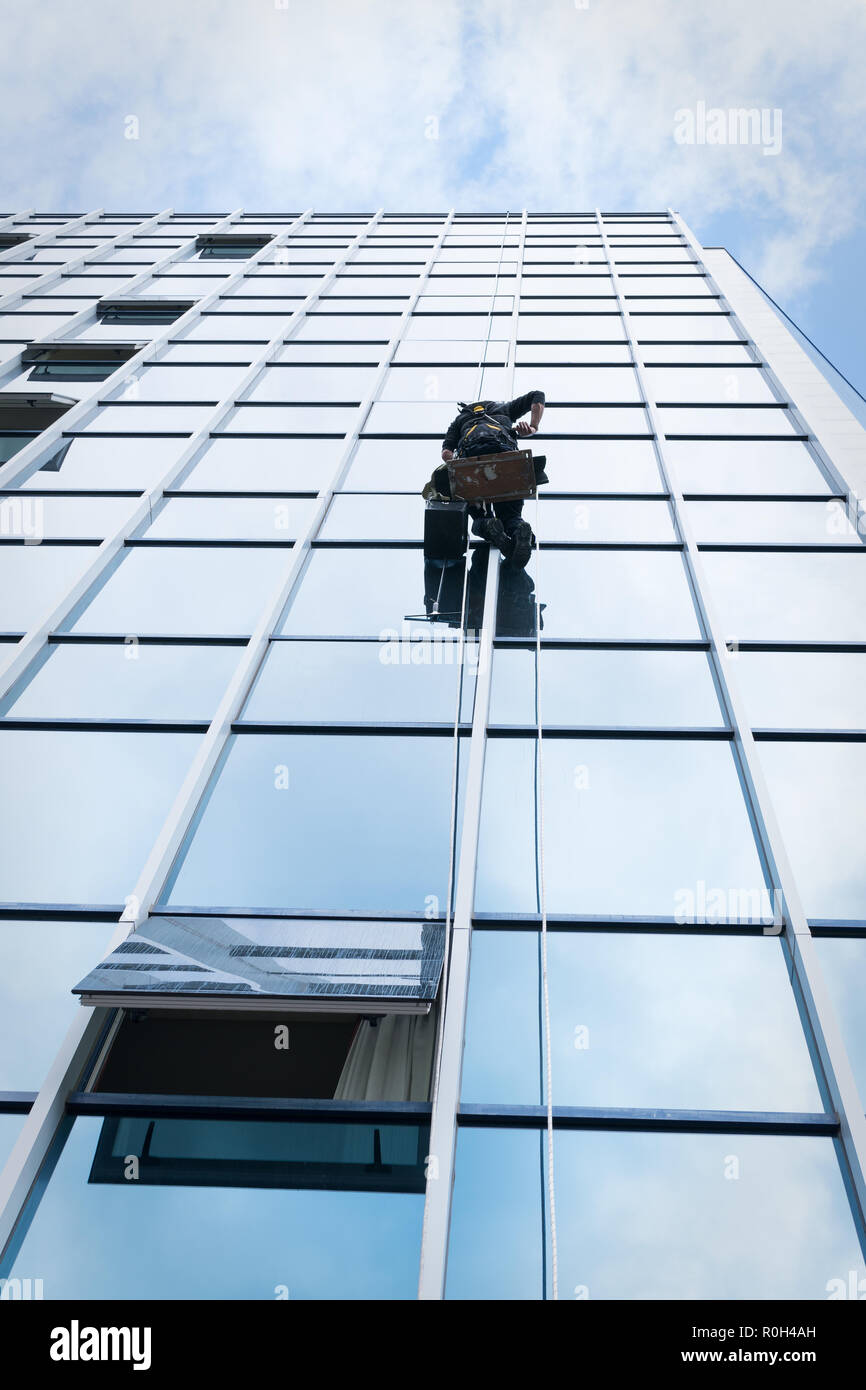 Nettoyant à travailler sur une façade de verre suspendue Banque D'Images