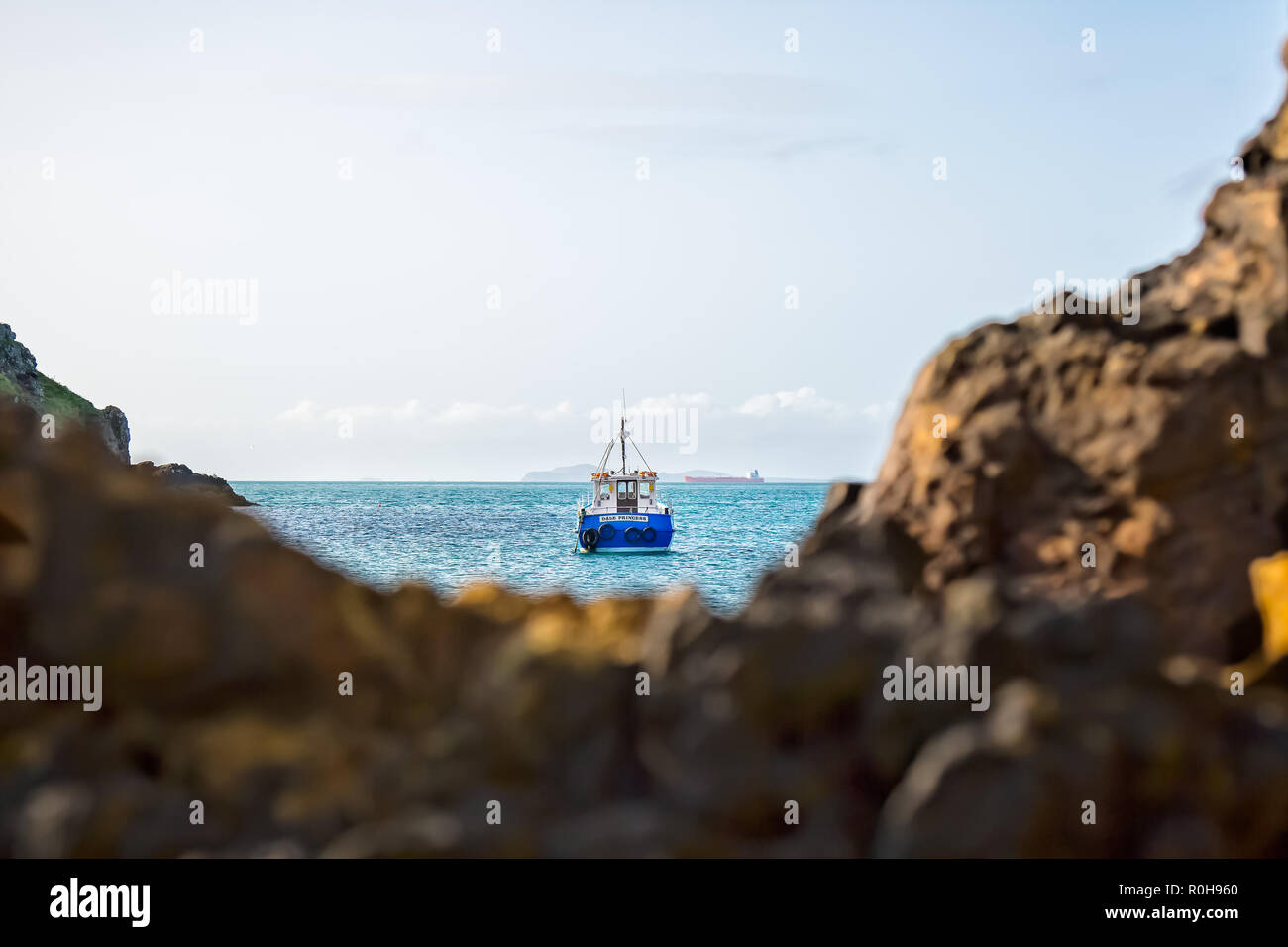 Capture Paysage de bateau en mer, ancré dans la crique, à l'intermédiaire de soft-focus craggy rochers en premier plan, à partir de la plage. L'île de Skomer bateau de débarquement. Banque D'Images