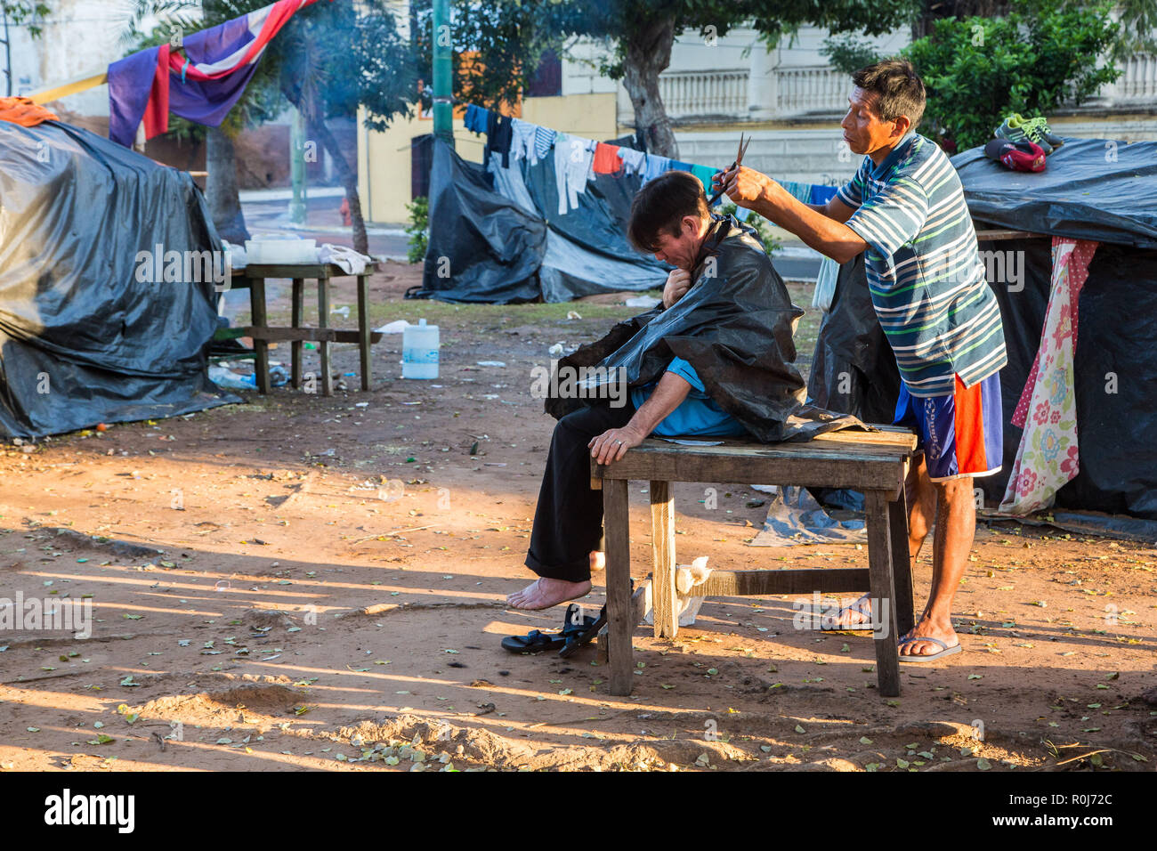 Coupe de l'extérieur dans des bidonvilles de la ville d'Asuncion. La coiffure dans les rues de Ciudad de Asunción au Paraguay. Deux hommes, camp de toile. Banque D'Images