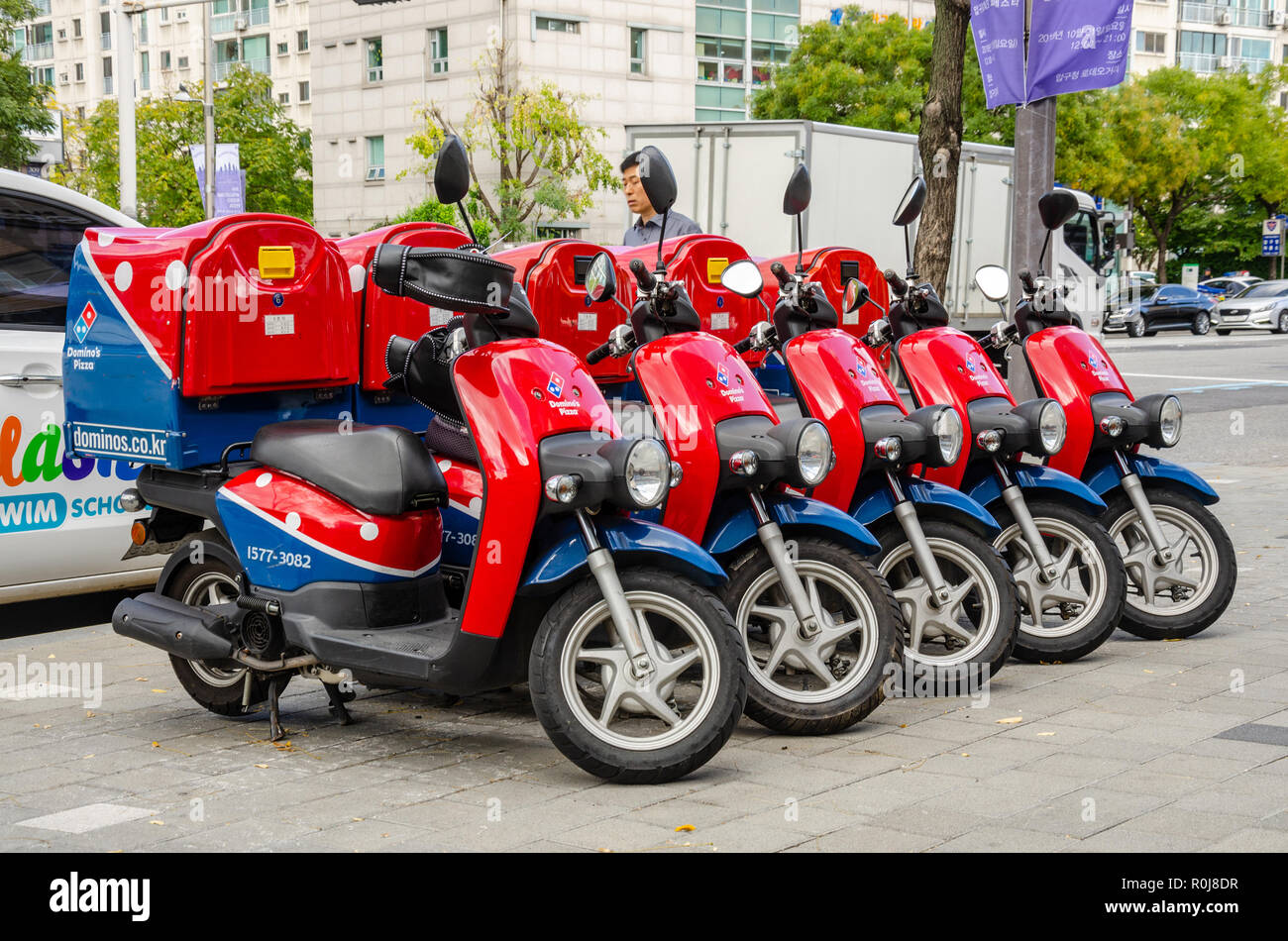 Rouge et bleu livraison scooters cyclomoteur Dominos soigneusement garé dans une ligne sur un trottoir à Séoul, Corée du Sud. Banque D'Images