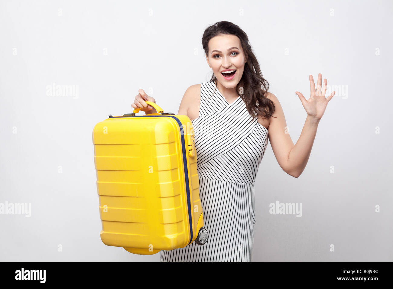 Portrait of happy young voyageur en robe rayée jaune valise debout et tenant à pleines dents accueil sourire et prêt pour les vacances. Piscine Banque D'Images