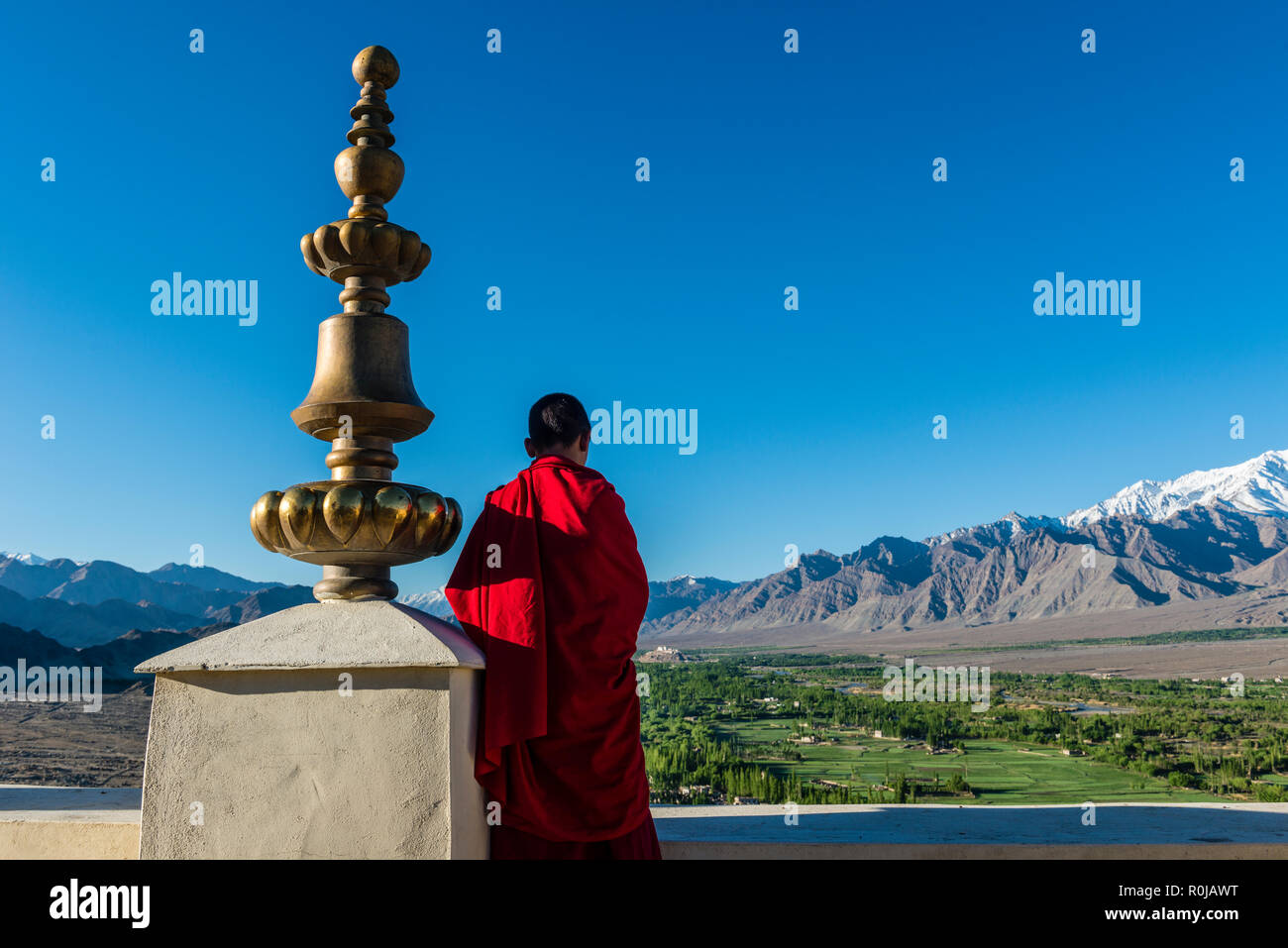 Un moine habillé rouge à la verte jusqu'à la vallée de l'Indus du toit de Thiksey Gompa, un des plus importants monastères du Ladakh Banque D'Images