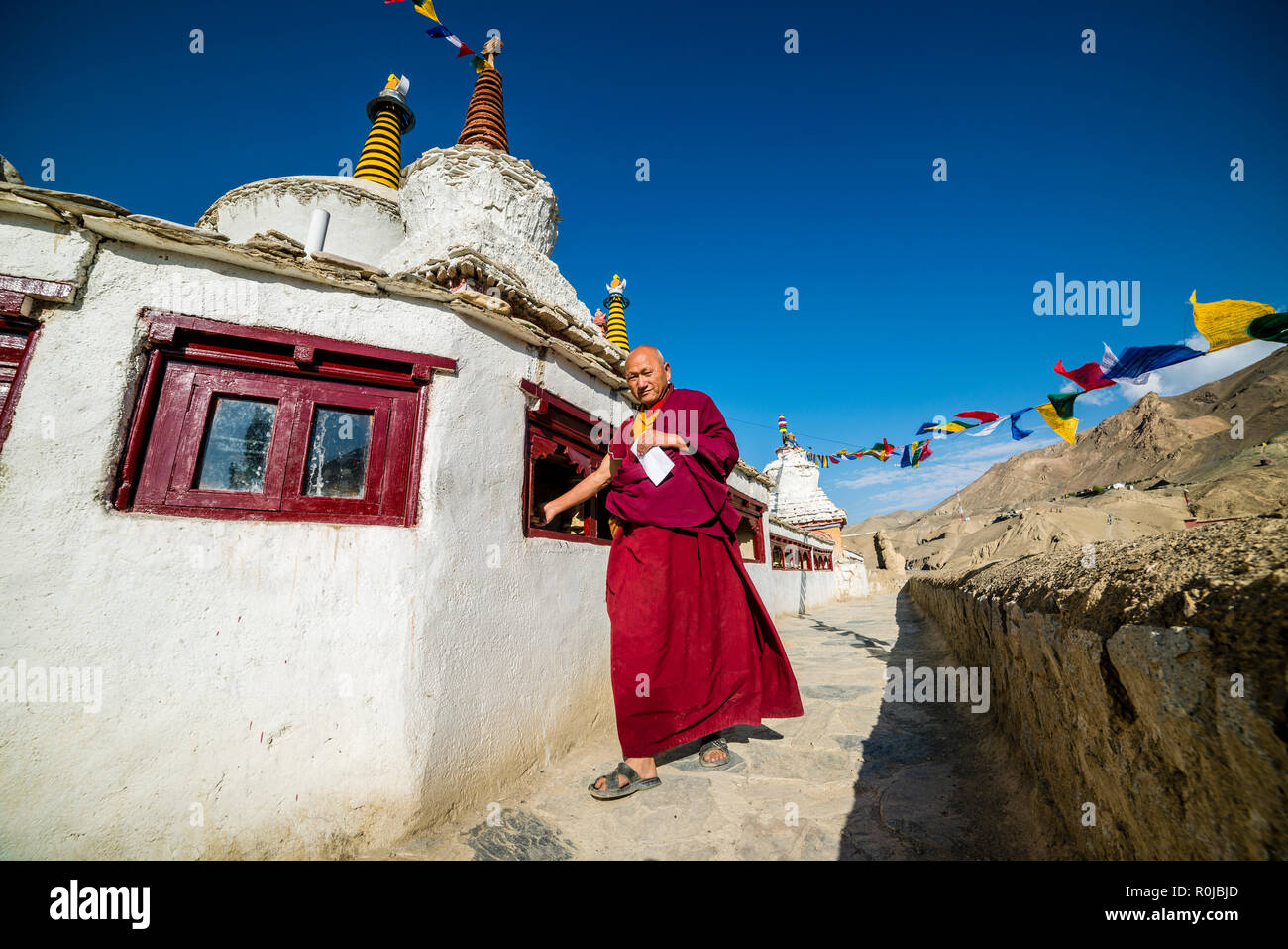 Un moine, vêtu de rouge, est de marcher autour de Lamayuru Gompa, le plus ancien et le plus grand monastère existant au Ladakh, en tournant les roues de prière pour relige Banque D'Images