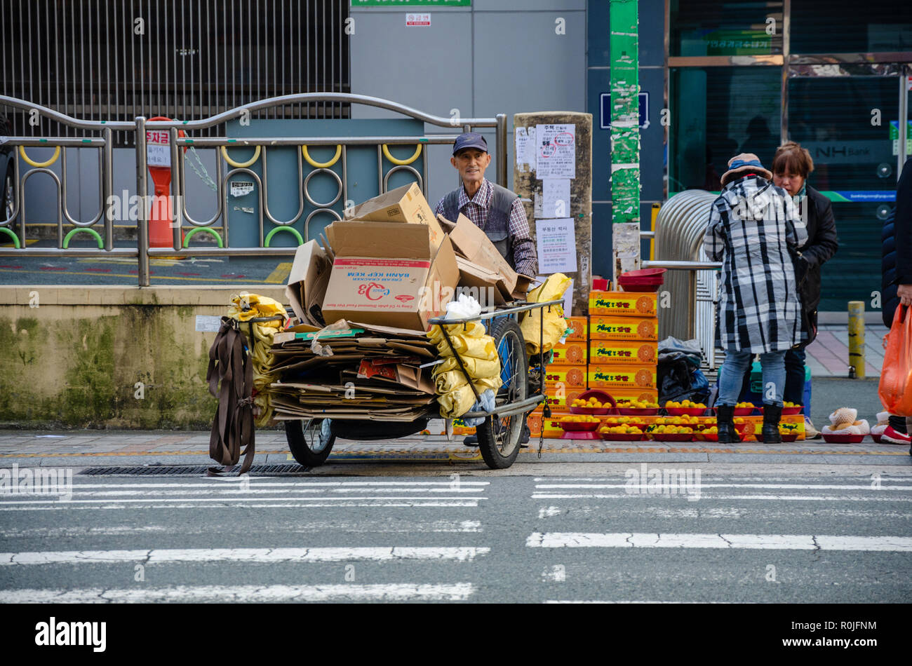 Un homme pousse un chariot à travers une zone piétonne qui est chargé avec de vieilles boîtes en carton. Banque D'Images