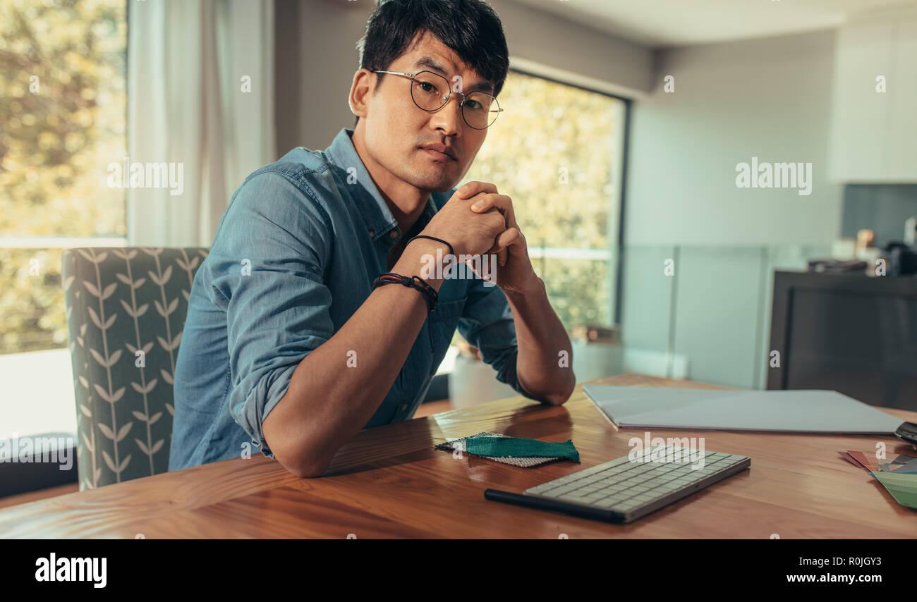 Portrait de creative est l'homme assis à un bureau avec clavier de l'ordinateur et d'échantillons de tissus. Architecte confiant à son bureau à la recherche à l'appareil photo. Banque D'Images