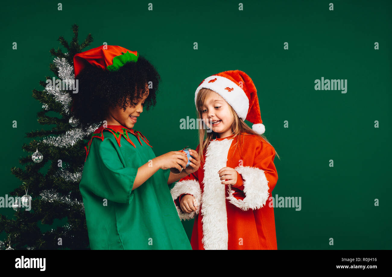 Enfants heureux en jouant avec leurs costumes de Noël cadeaux de Noël. Enfants multiethnique à un jouet à debout à côté d'un arbre de Noël décoré. Banque D'Images