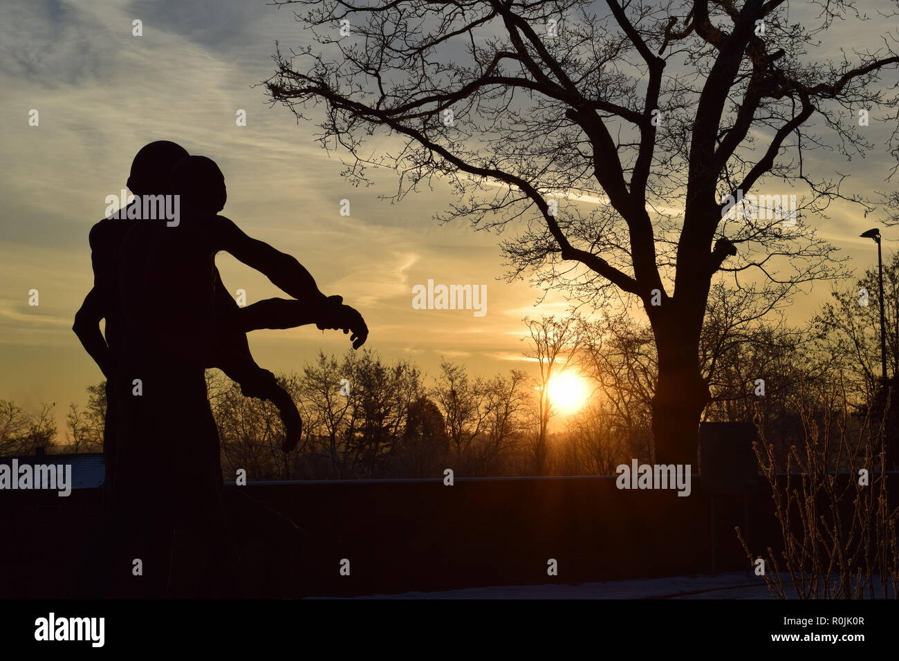 Chronologie du soleil levant au cours de l'hiver tombée de ciel vu de derrière la sculpture de bronze au cimetière militaire Reimsbach an der Saar, Allemagne. Banque D'Images