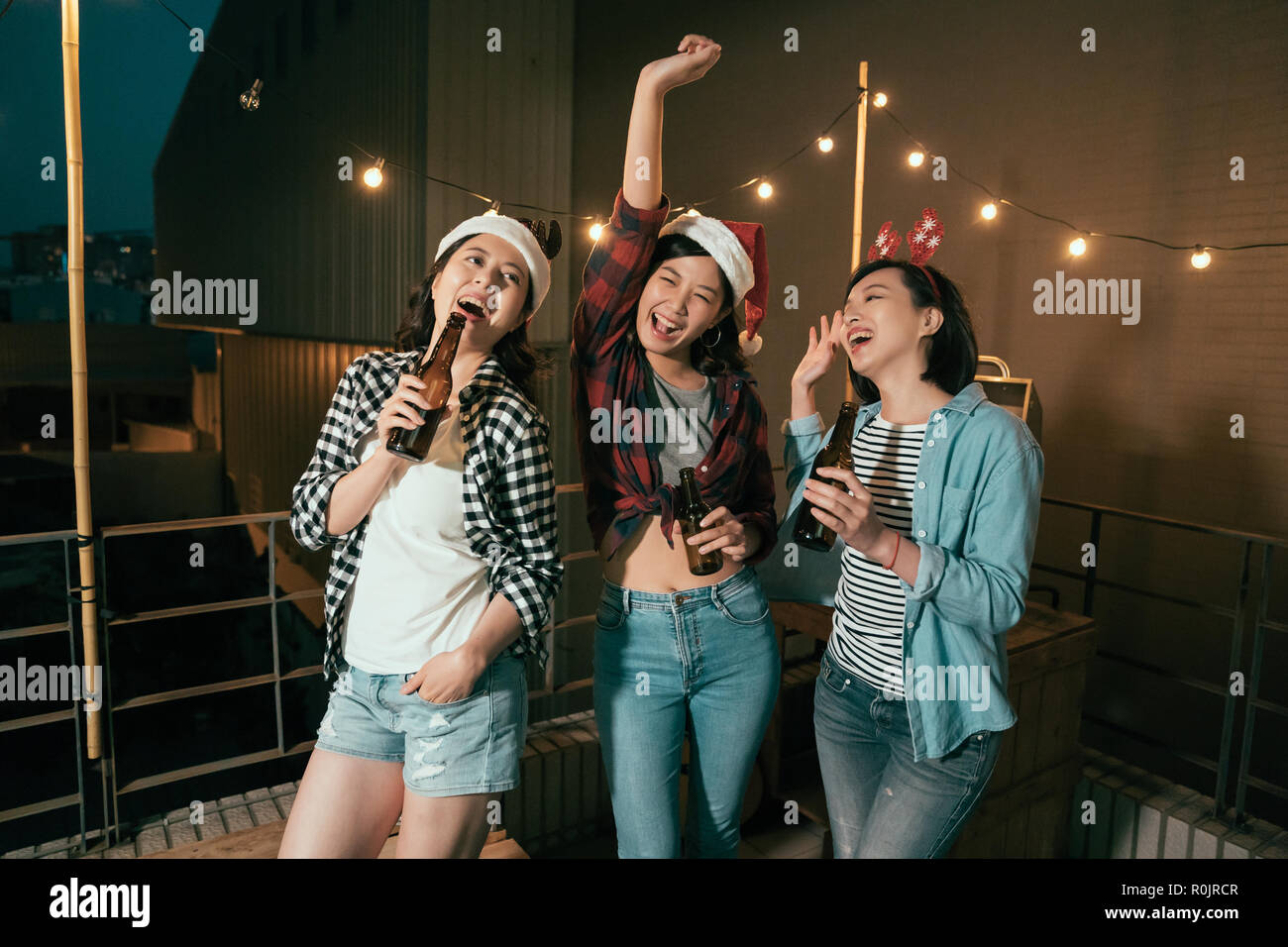 Les jeunes filles dansant sombre nuit fête de Noël à l'extérieur. cheerful mesdames avec des alcools bières profitez de la musique sur le balcon. Les copines sans souci sur le toit te Banque D'Images