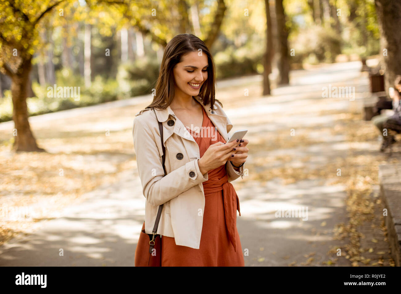 Happy young woman using cell phone in autumn park sur belle journée Banque D'Images