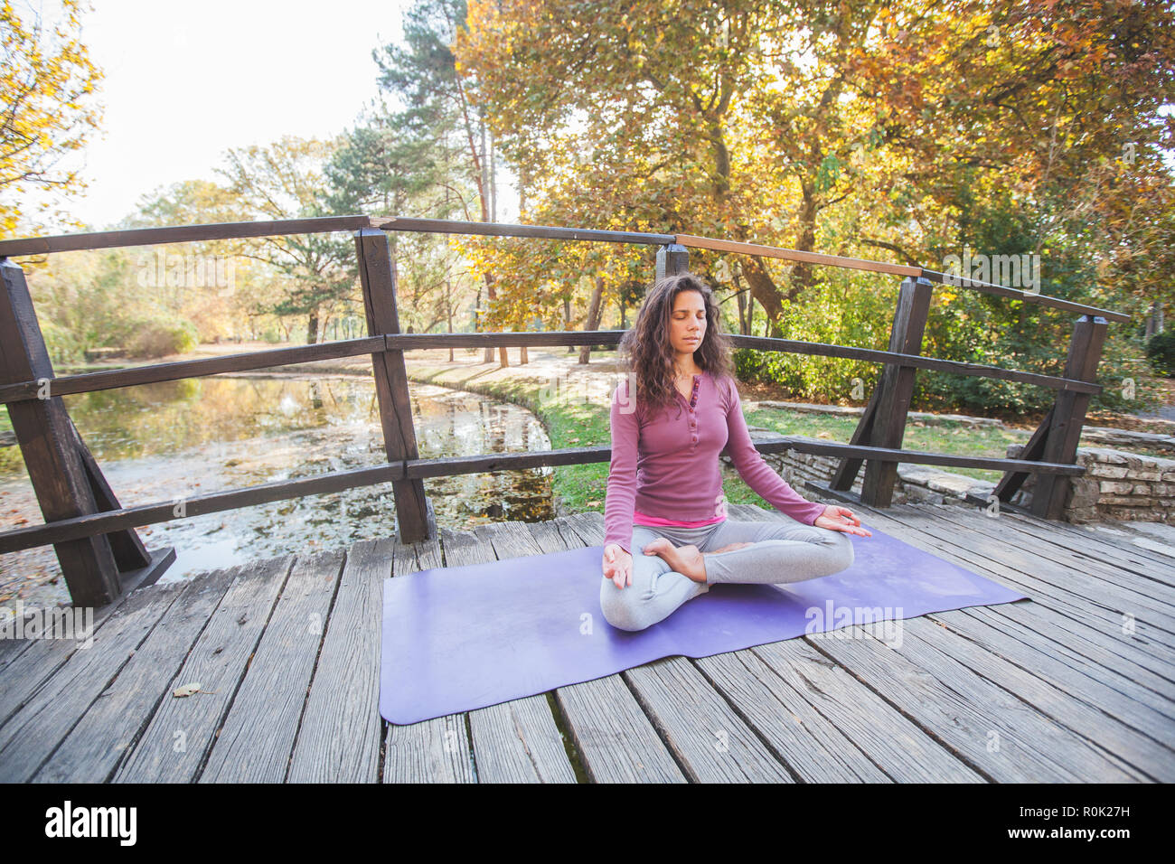 Femme méditant et en pratiquant le Yoga, Lotus pose, le Padmasana. Méditation sur la journée ensoleillée d'automne sur le pont de bois dans la région de City Park. Banque D'Images