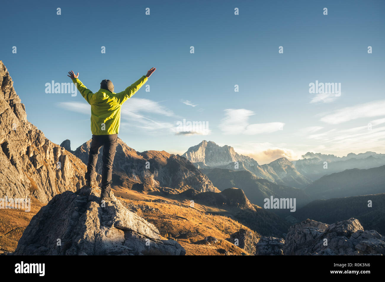 Homme debout sportive sur la pierre avec les armes contre mountain valley au coucher du soleil. Heureux jeune homme, rochers, forêt d'automne et ciel bleu dans la dolomie Banque D'Images