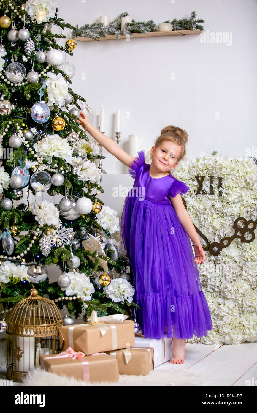 Jolie petite fille de 4 ans dans une robe bleue. Bébé en chambre de Noël  avec teddybear, grosse horloge, arbre de Noël, marron fauteuil, bougies et  cadeaux Photo Stock - Alamy