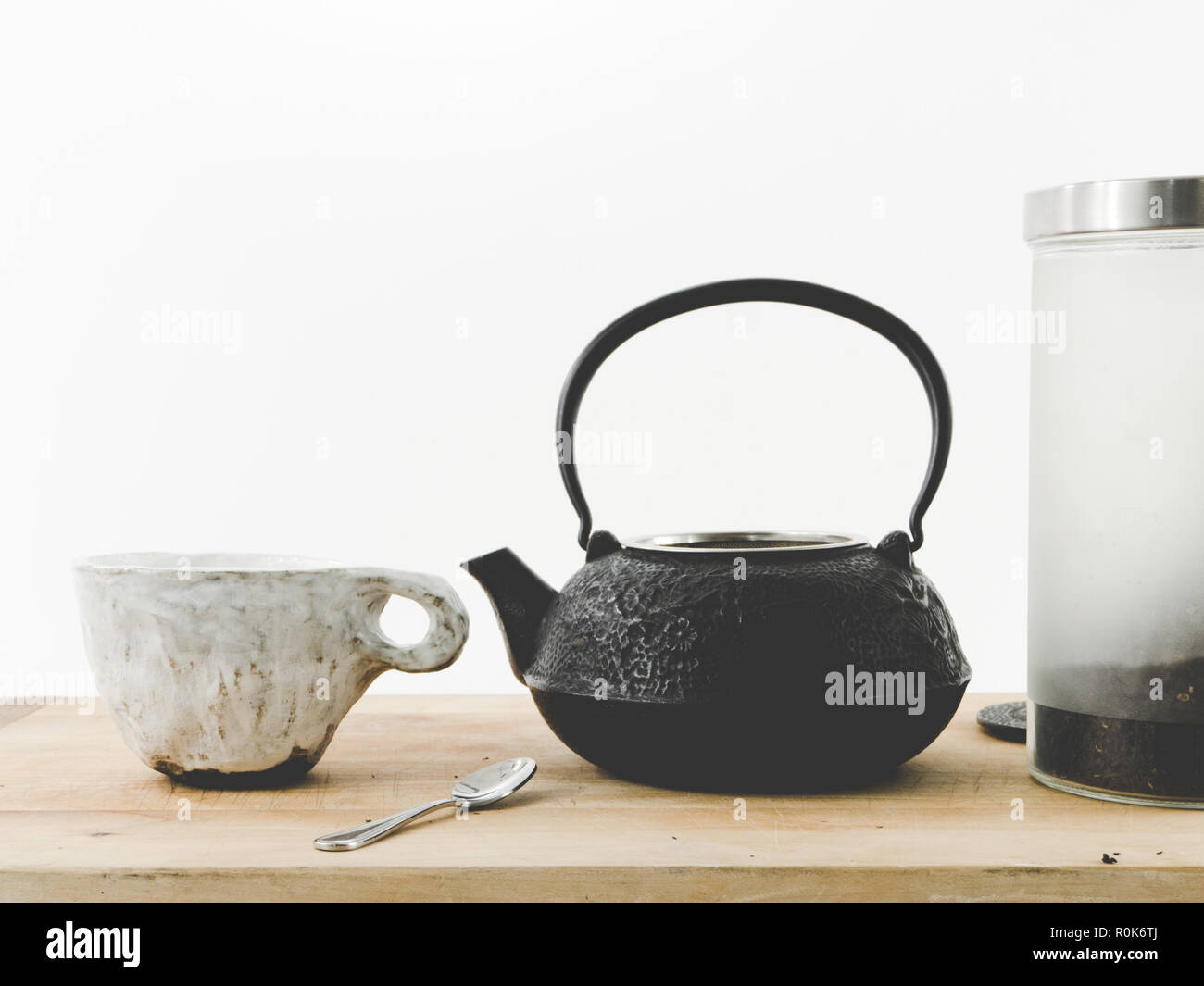 Théière en fonte avec cannister de thé noir et de céramique faite à la main / tasse mug sur un plateau en bois pâle fond blanc avec des prix pour la copie. Hygge. Banque D'Images