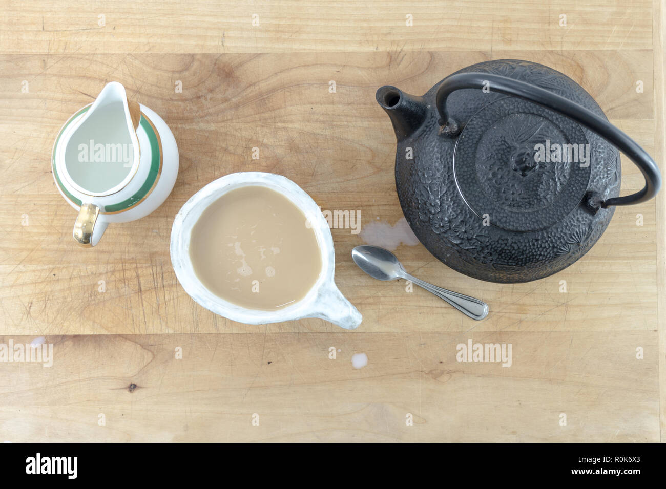 Vue de dessus en fonte noire théière avec tasse de thé chaud et pitcher de crème et une cuillère sur une table en bois ou le bac. Banque D'Images