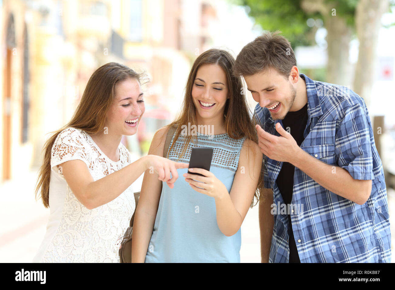 Trois amis heureux de regarder le contenu du smartphone dans la rue Banque D'Images
