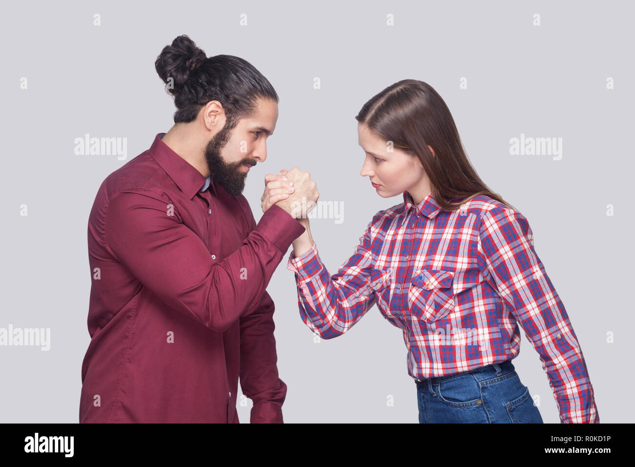 Vue côté profil portrait de l'homme et la femme à barbe style casual debout dans armwrestling poser et se regardant avec sérieux. Banque D'Images
