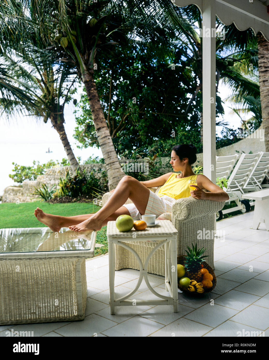 Jeune femme se détendre dans un fauteuil en rotin blanc, terrasse, jardin tropical, palmiers, Guadeloupe, French West Indies, Banque D'Images