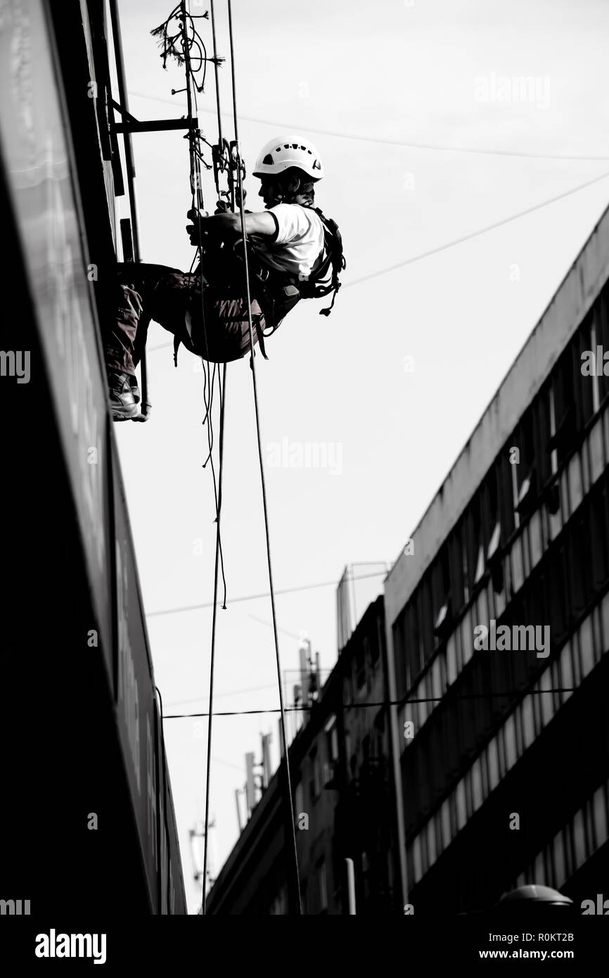 Belgrade, Serbie - 19 novembre 2018 : Industrial climber hanging on a rope lors de l'installation sur une bannière publicitaire bilding, low angle view dans blac Banque D'Images