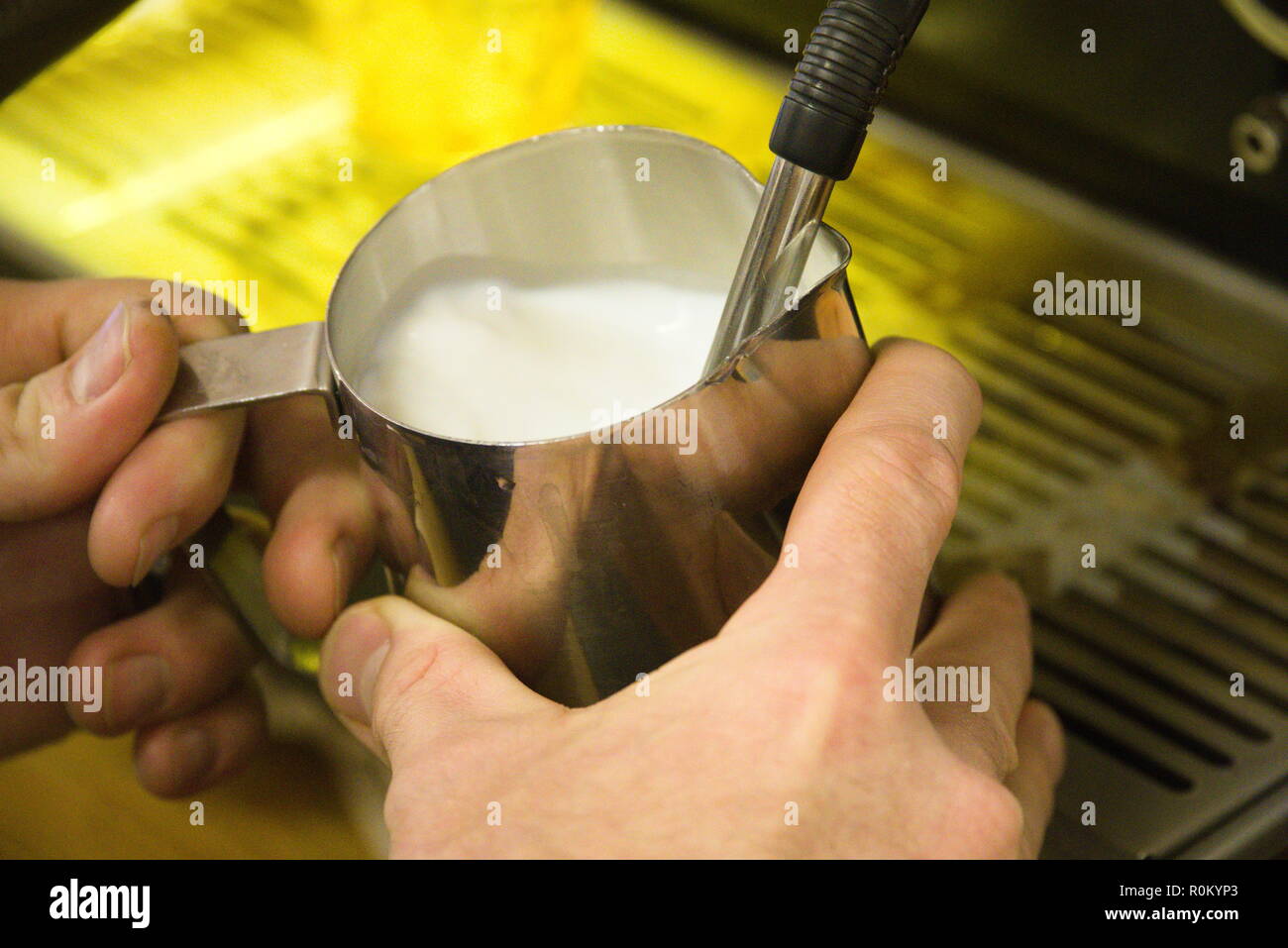 Un barista verse du lait chaud dans un récipient à partir d'une machine. Banque D'Images