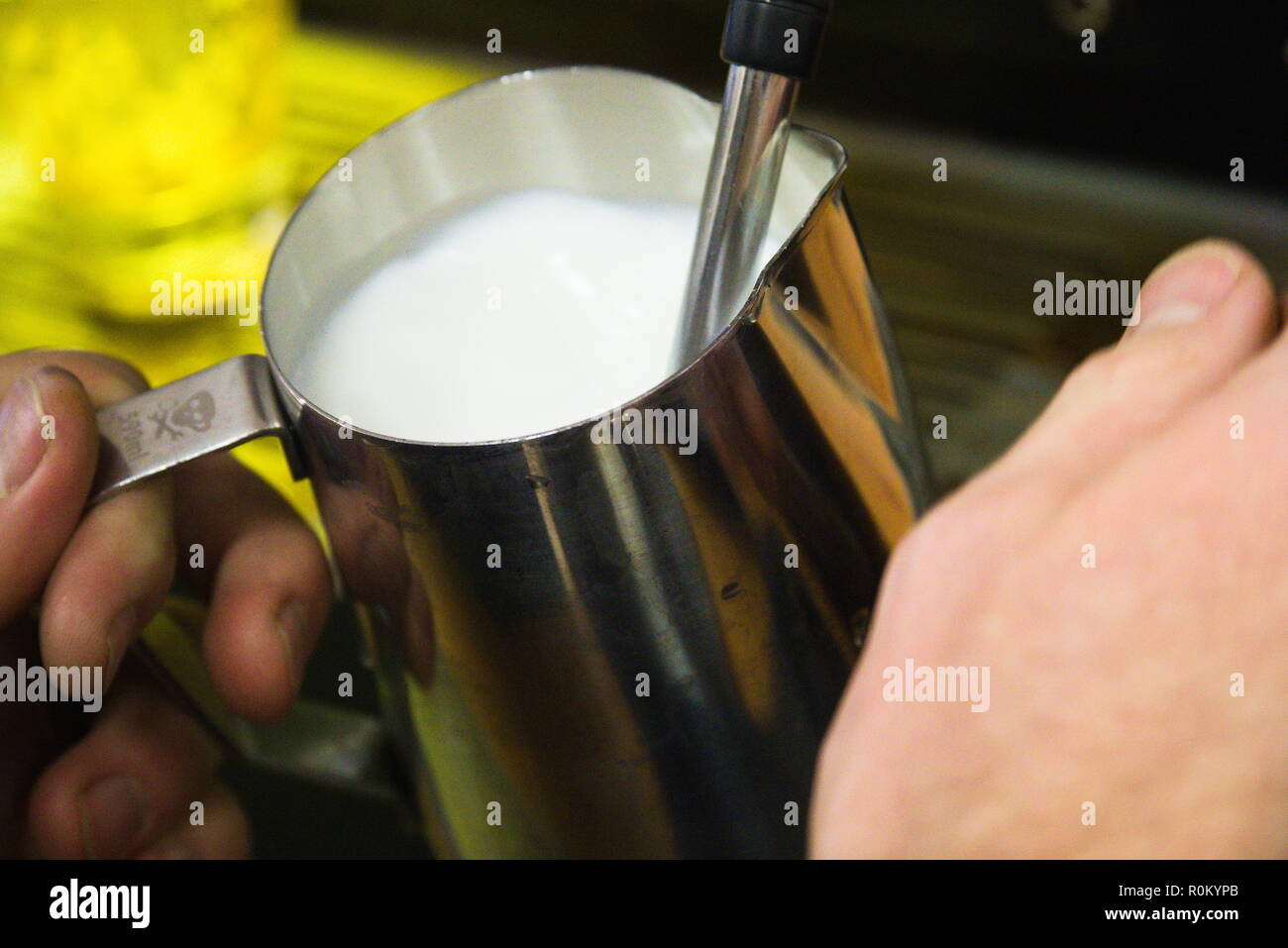 Un barista verse du lait chaud dans un récipient à partir d'une machine. Banque D'Images