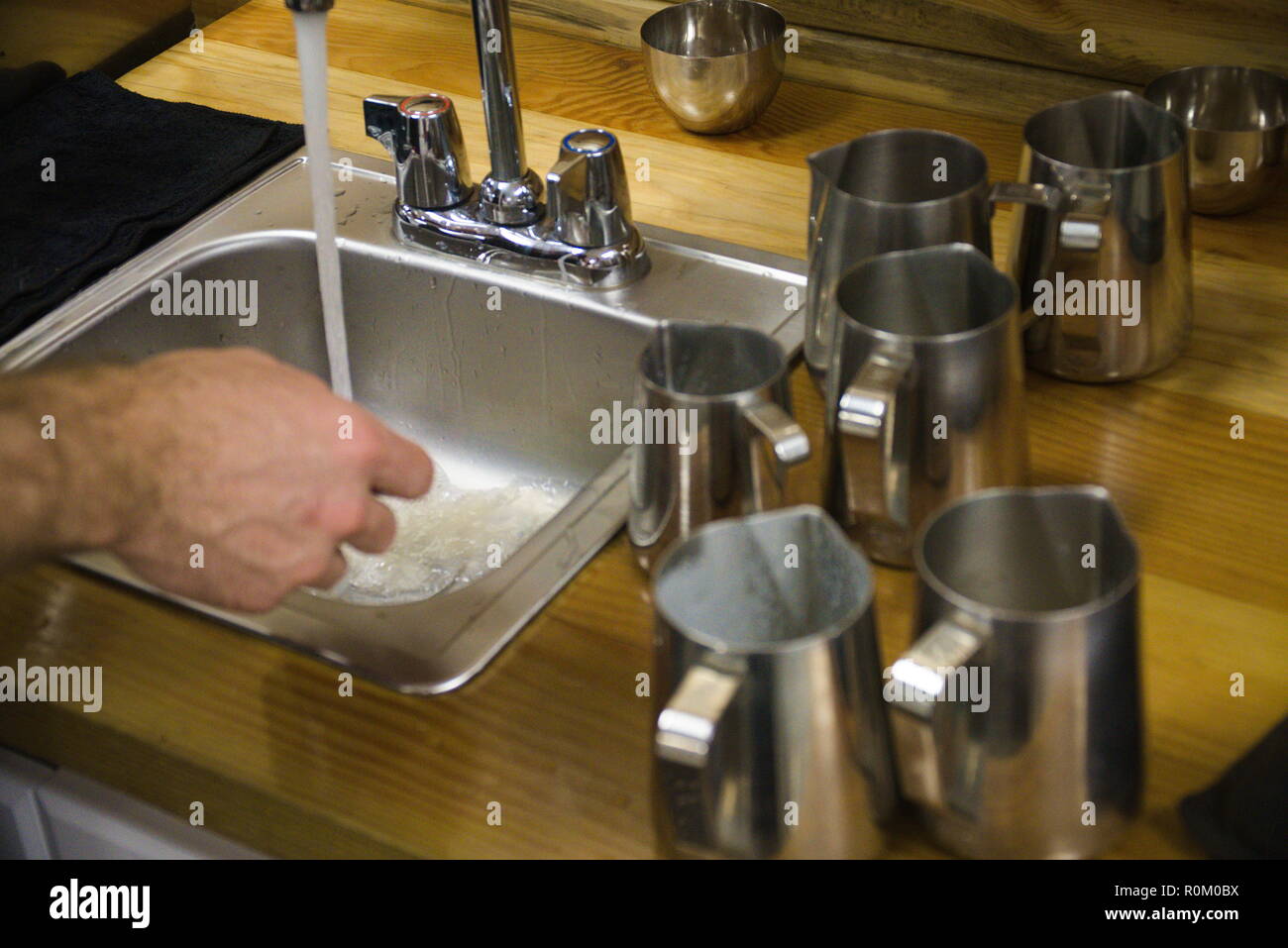Un barista se lave les mains dans un évier. Sur la droite il y a des capsules métalliques. Banque D'Images