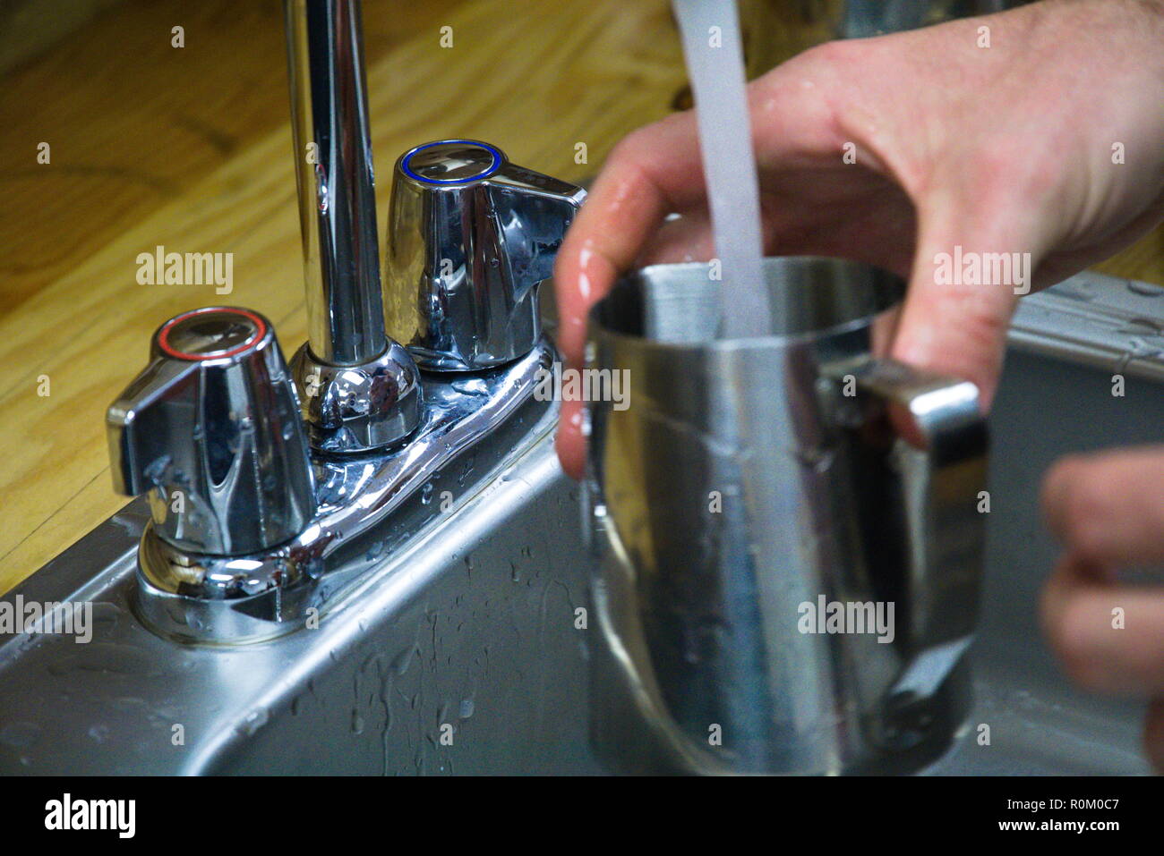 Un barista est titulaire d'un gobelet de métal comme l'eau d'un lavabo en métal est affluaient dans. Banque D'Images
