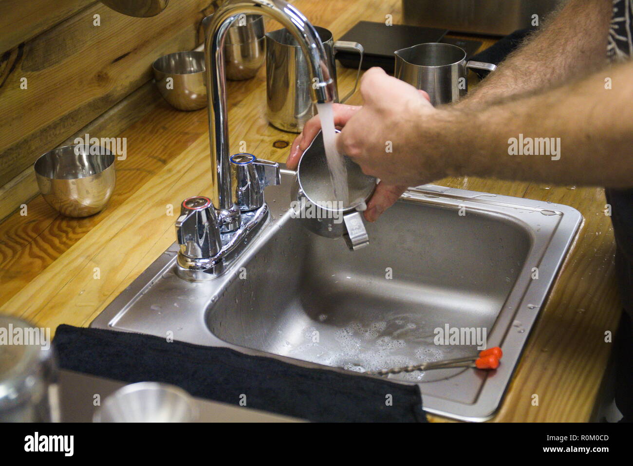 Un barista lave un metal becher dans un évier avec de l'eau couler. Banque D'Images