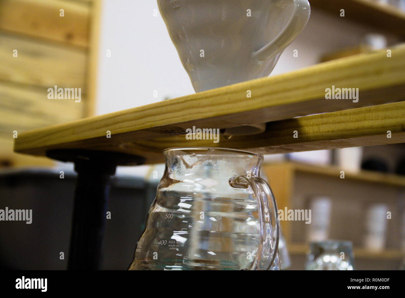 Une tasse à café est assis sur une poutre en bois sur un pot en verre. Le Barista fait verser sur le café. Banque D'Images