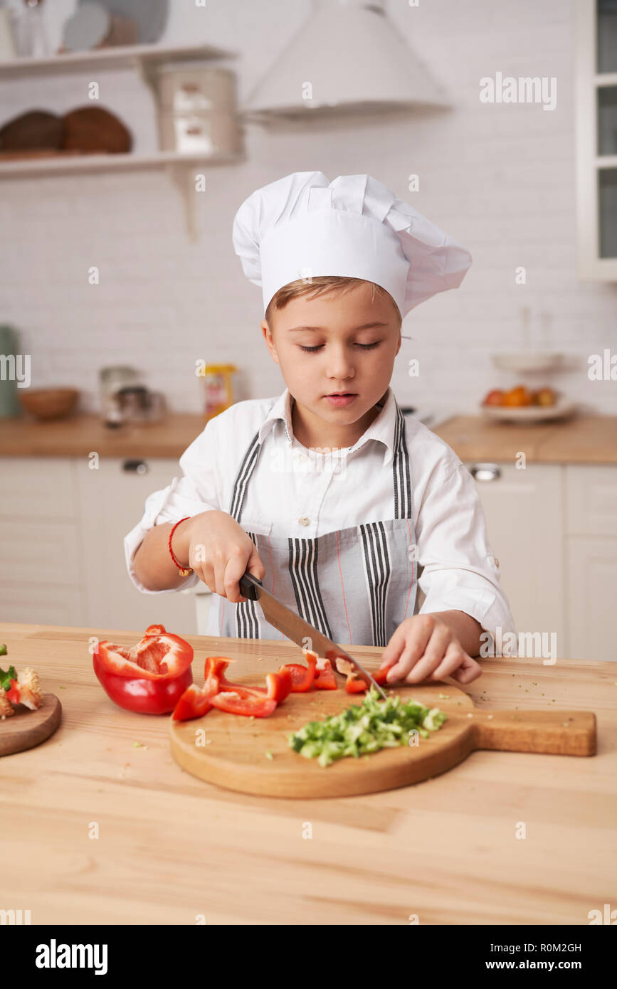 Cute little boy dans la cuisine moderne équipée à la maison. Garçon cuire les légumes. Banque D'Images