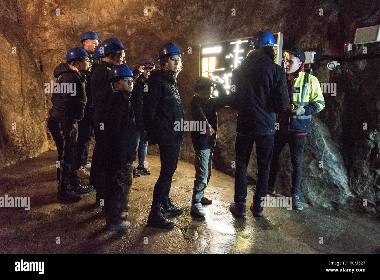 Un groupe de visiteurs portant des casques de sécurité, se rassemblent autour de leur guide dans une grande veste vis, montrant un illuminé plan de la cavité souterraine système dans Banque D'Images